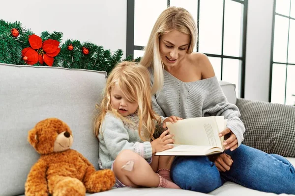 母亲和女儿坐在家里的圣诞装饰品旁看书 — 图库照片