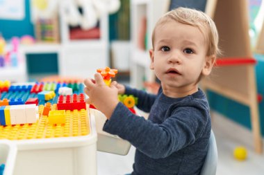 Anaokulundaki masada oturan sevimli sarışın çocuk inşaat bloklarıyla oynuyor.