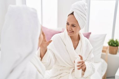 Two women mother and daughter wearing bathrobe applying skin treatment at bedroom