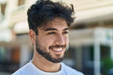 Young hispanic man smiling confident looking to the side at street
