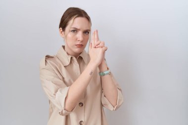 Young caucasian woman wearing casual shirt holding symbolic gun with hand gesture, playing killing shooting weapons, angry face 