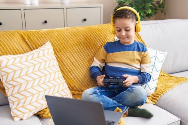 Adorable hispanic boy playing video game sitting on sofa at home