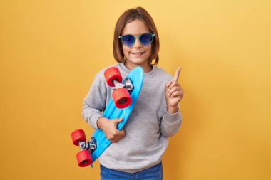 Küçük İspanyol çocuk güneş gözlüğü takıyor, gülümsüyor, mutlu bir şekilde elini ve parmağını yana doğru gösteriyor. 