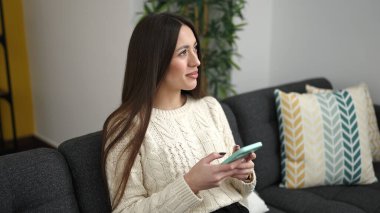 Evdeki kanepede oturan akıllı telefon kullanan genç, güzel İspanyol kadın.