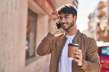 Genç İspanyol adam akıllı telefonda konuşuyor. Sokakta kahve içiyor.