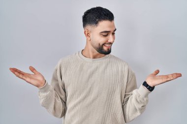 Young handsome man standing over isolated background smiling showing both hands open palms, presenting and advertising comparison and balance 