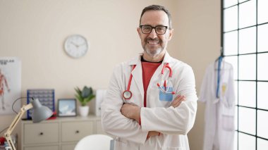 Middle age man doctor smiling confident standing with arms crossed gesture at clinic