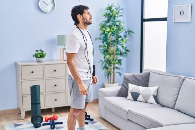 Handsome latin man wearing sportswear at home looking to side, relax profile pose with natural face with confident smile. 