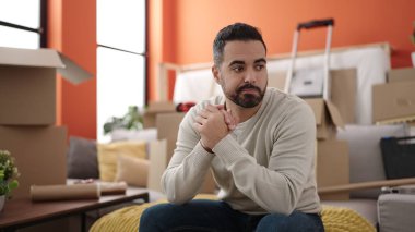 Young hispanic man sitting on sofa with relaxed expression at new home