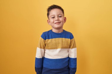Little hispanic boy standing over yellow background with a happy and cool smile on face. lucky person. 