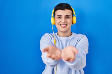 Non binary person listening to music using headphones smiling with hands palms together receiving or giving gesture. hold and protection 