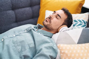 Young hispanic man listening to music sleeping on sofa at home