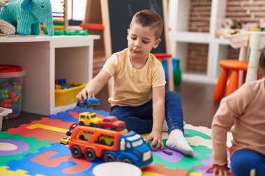 Two kids playing with cars toy sitting on floor at kindergarten