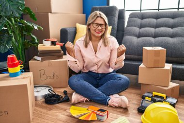Young hispanic woman moving to a new home sitting on the floor excited for success with arms raised and eyes closed celebrating victory smiling. winner concept. 