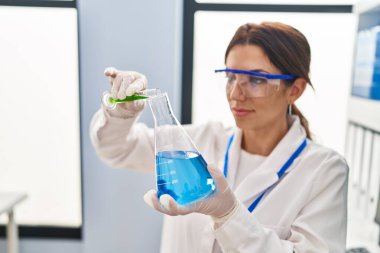 Laboratuvarda sıvı ölçen bilim adamı üniforması giyen genç İspanyol kadın.