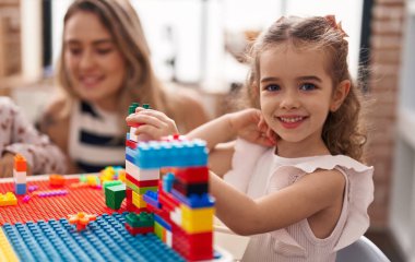 Teacher and toddler playing with construction blocks sitting on table at kindergarten