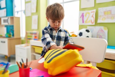 Anaokulunda duran sevimli İspanyol çocuk sırt çantası kitabını tutuyor.