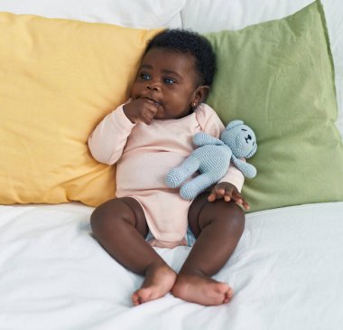 African american baby sitting on bed sucking hand at bedroom