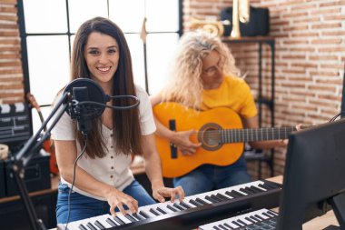 İki kadın müzisyen müzik stüdyosunda klasik gitar ve piyano çalarak şarkı söylüyor.