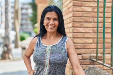 Orta yaşlı İspanyol kadın sokakta kendine güvenerek gülümsüyor.