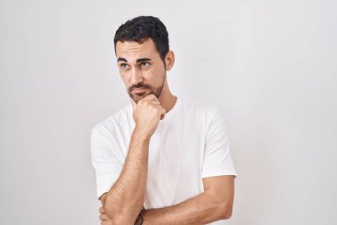 Handsome hispanic man standing over white background thinking worried about a question, concerned and nervous with hand on chin 