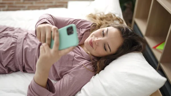 年轻美丽的惊慌失措的女人用智能手机躺在卧室的床上 — 图库照片