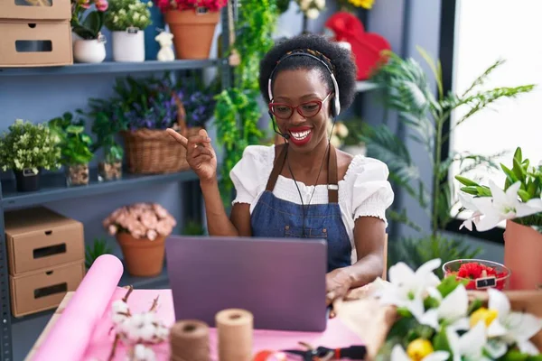 African woman with curly hair working at florist shop doing video call smiling happy pointing with hand and finger to the side