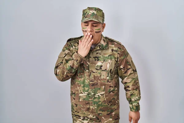Hispanic young man wearing camouflage army uniform bored yawning tired covering mouth with hand. restless and sleepiness.