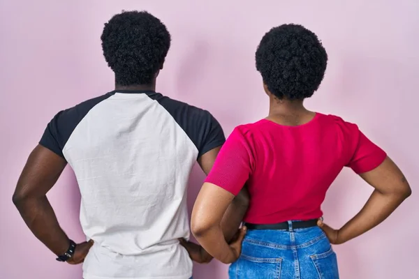 若いですアフリカ系アメリカ人のカップル立っていますピンクの背景の上に後ろに立っています離れて腕で体 — ストック写真
