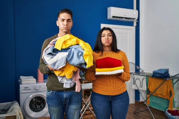 Young Couple Holding Laundry Dirty Clean Laundry Puffing Cheeks Funny — Zdjęcie stockowe