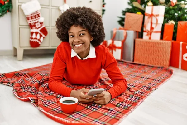 Young African American Woman Using Smartphone Lying Christmas Tree Home — Fotografia de Stock