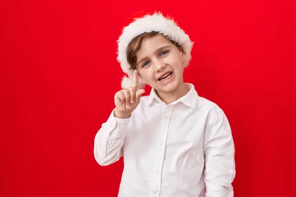 头戴红底圣诞帽 头戴圣诞礼帽 头戴圣诞礼帽的高加索小男孩笑着提出了一个想法或问题 满脸喜形于色地点点头 位居第一 — 图库照片
