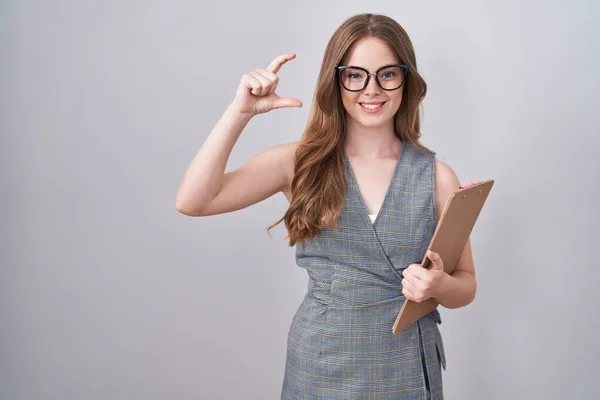 Caucasian woman wearing glasses and business clothes smiling and confident gesturing with hand doing small size sign with fingers looking and the camera. measure concept.