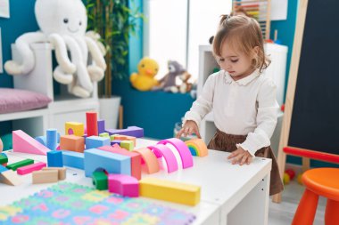 Adorable blonde girl playing with toys standing at kindergarten