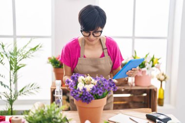 Middle age chinese woman florist smiling confident using touchpad at flower shop