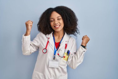 Doktor üniforması ve steteskop giyen genç Afro-Amerikan kadın kolları açık ve gözleri kapalı bir şekilde başarıyı kutluyor ve şaşırıyor. Kazanan konsept. 