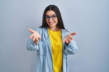 Mavi arka planda duran genç İspanyol kadın gülümseyen, yardım eli uzatan ve kabullenen. 