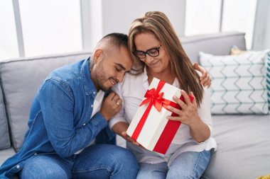 Man and woman mother and son surprise with gift hugging at home