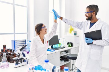 Man and woman scientist partners holding clipboard high five raised up hands at laboratory