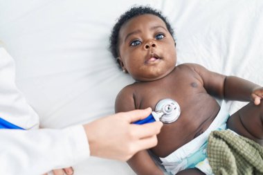 African american baby having medical examination lying on bed at bedroom