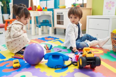 Two kids playing with toys sitting on floor at kindergarten
