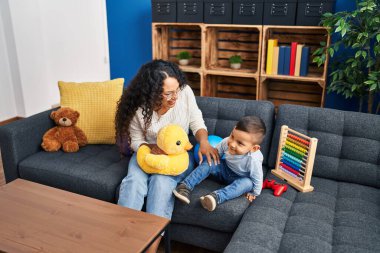 Mother and son playing with toys sitting on sofa at home