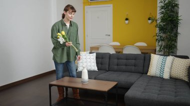 Young caucasian woman putting flowers in a vase at home