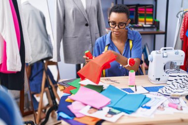 Terzi dükkanında elinde kumaş ve iplik tutan Afrikalı Amerikalı bir kadın.