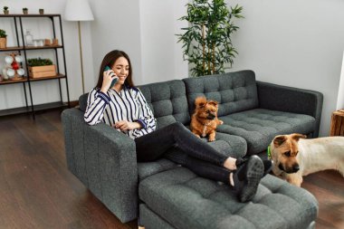 Genç İspanyol kadın akıllı telefonda konuşuyor. Kanepede oturuyor, evde köpeklerle.
