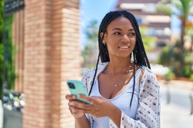 Afro-Amerikalı kadın sokakta akıllı telefon kullanarak kendine güveniyor.