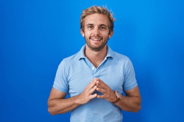 Beyaz adam mavi arka planda el ele tutuşup gülümseyerek rahatça ve neşeyle gülümsüyor. Başarı ve iyimserlik 