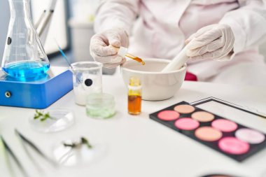 Genç İspanyol kadın bilim adamı üniforması giyiyor. Laboratuvarda kaseye sıvı döküyor.