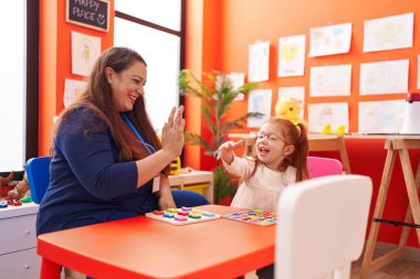 Teacher and student playing with maths puzzle game sitting on table at kindergarten