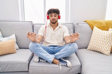 Young arab man doing yoga exercise sitting on sofa at home